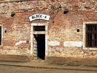 en:The facade of a building made of weathered red brick,with barred windows and an entrance bearing the inscription “BLOCK-A" ;fr:La façade d'un immeuble en briques rouges abimés,avec des fenêtres grillagées et une entrée portant l'inscription «BLOCK-A"