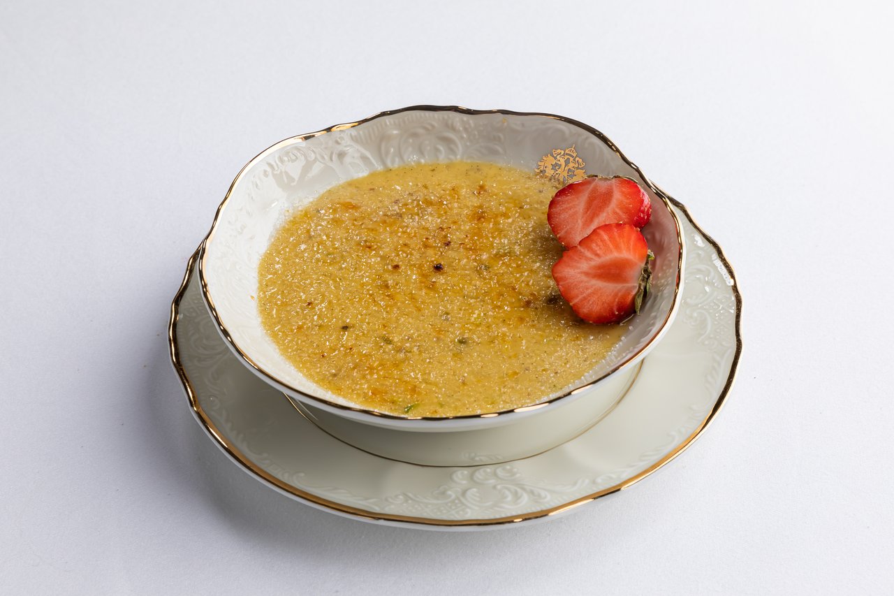 burnt cream served on white tableware adorned topped with two strawberries, served on white tableware adorned with gold and patterns