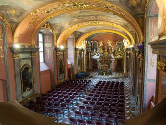 en:A long row of chairs in a chapel with colorful walls adorned with gold; fr:Grande rangée de chaise dans une chapelle aux murs colorées et ornées d'or