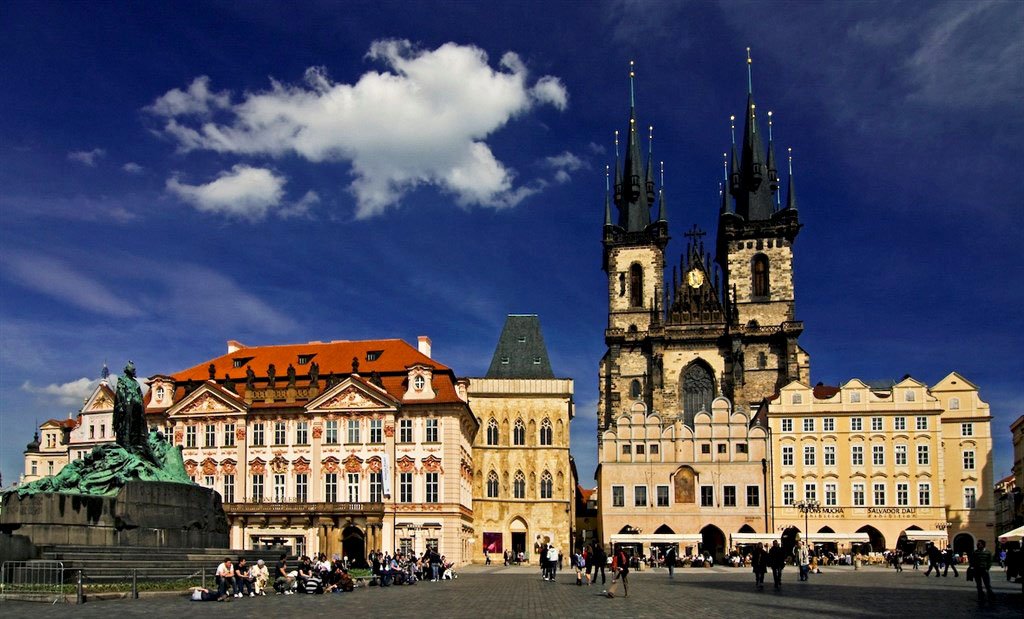 A large square, bustling with passersby and dominated by the palace and the church under a blue sky.