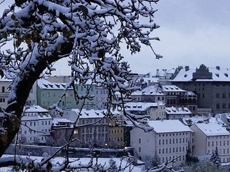 en:View of the snow-covered city, with Prague Castle lit up in the background; fr:Vue sur la ville enneigée, avec en arrière-plan le château de Prague illuminé