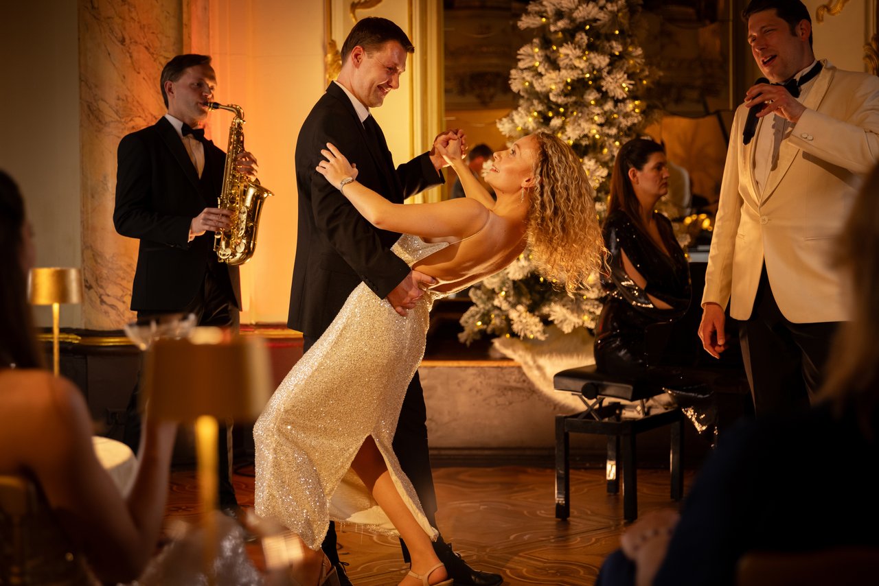 A woman in a white dress and a man in a black suit dancing with musicians in the background