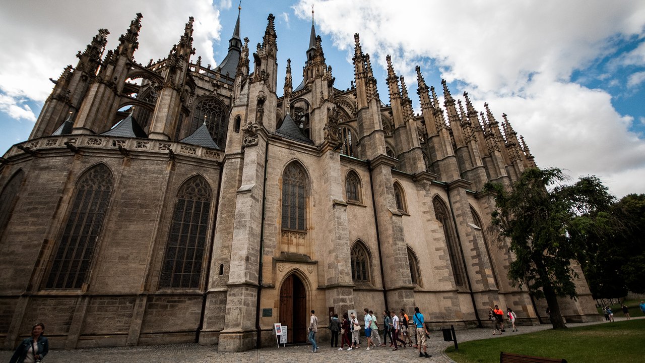 An imposing beige stone facade with a multitude of pointed, sculpted spires and large stained-glass windows