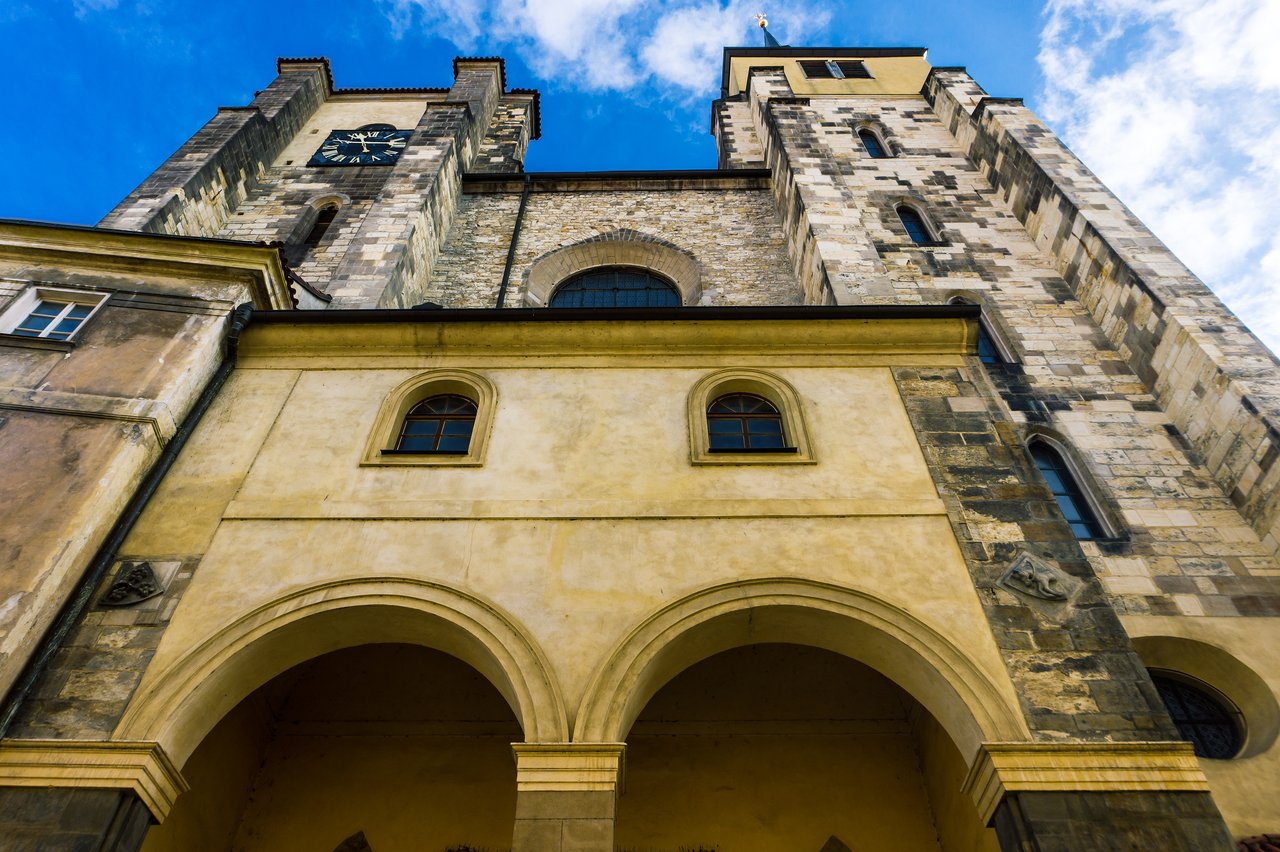 Exterior of a church with two towers, featuring a black-and-gold clock on the left tower